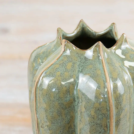 Close-up of a glossy ceramic vase with a scalloped rim, featuring a textured sage green and olive glaze with subtle gold-toned speckling and a thin gold line detail, set against a light wood background.