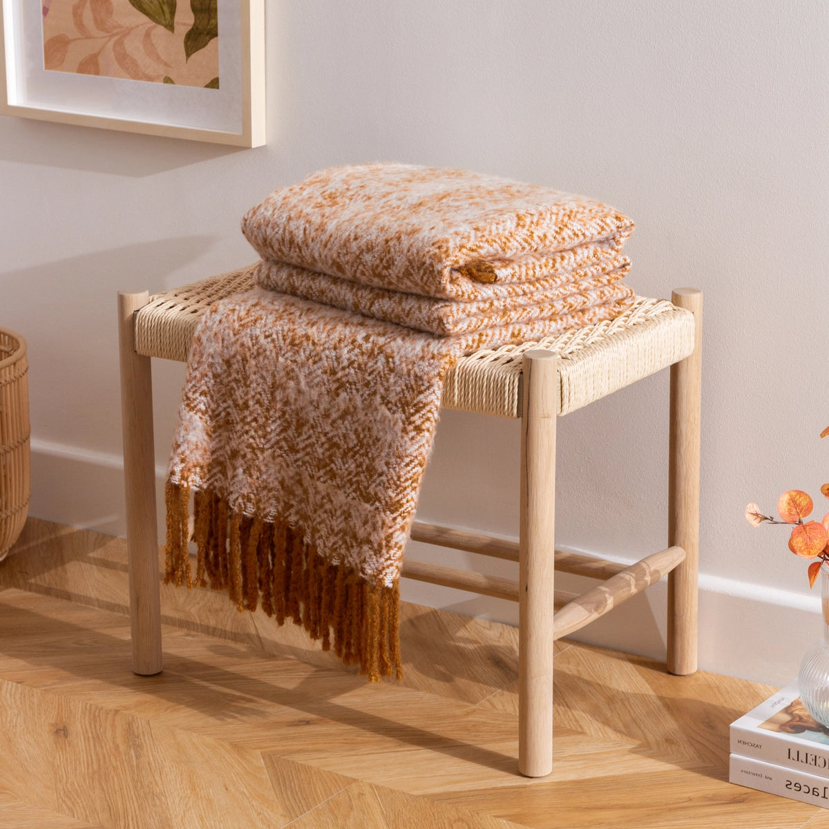 Folded golden blanket on a woven stool with a neutral wall and decor in the background