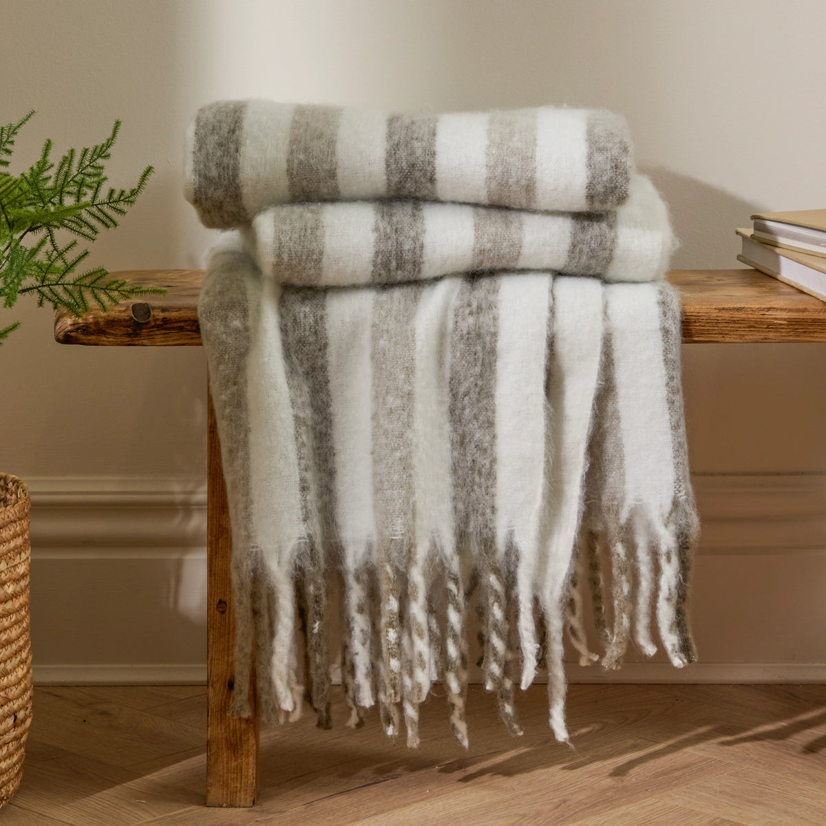 Striped blanket draped over a wooden bench with a plant and books in the background.