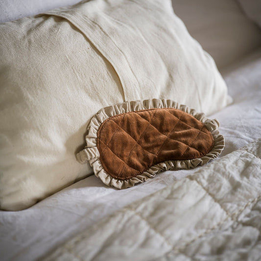 Brown plush eye mask on a white pillow and quilt
