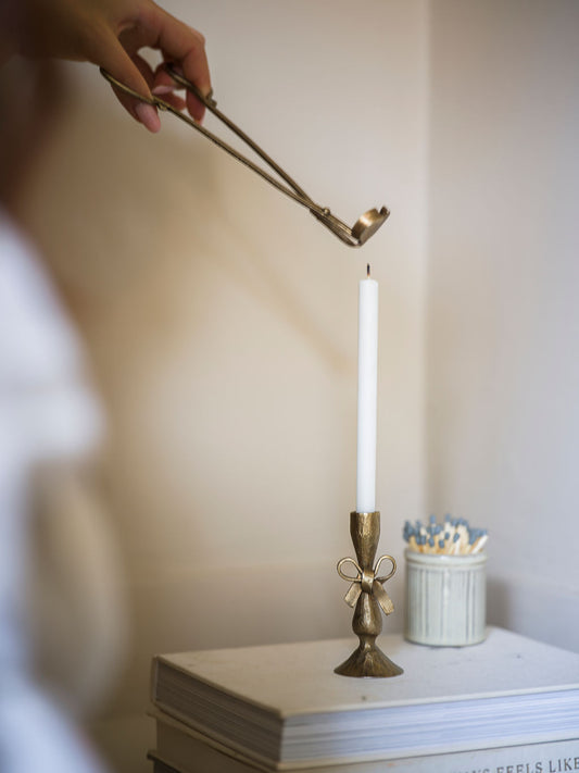 Person using wick trimmers to wick on a candle in a decorative holder on a surface.