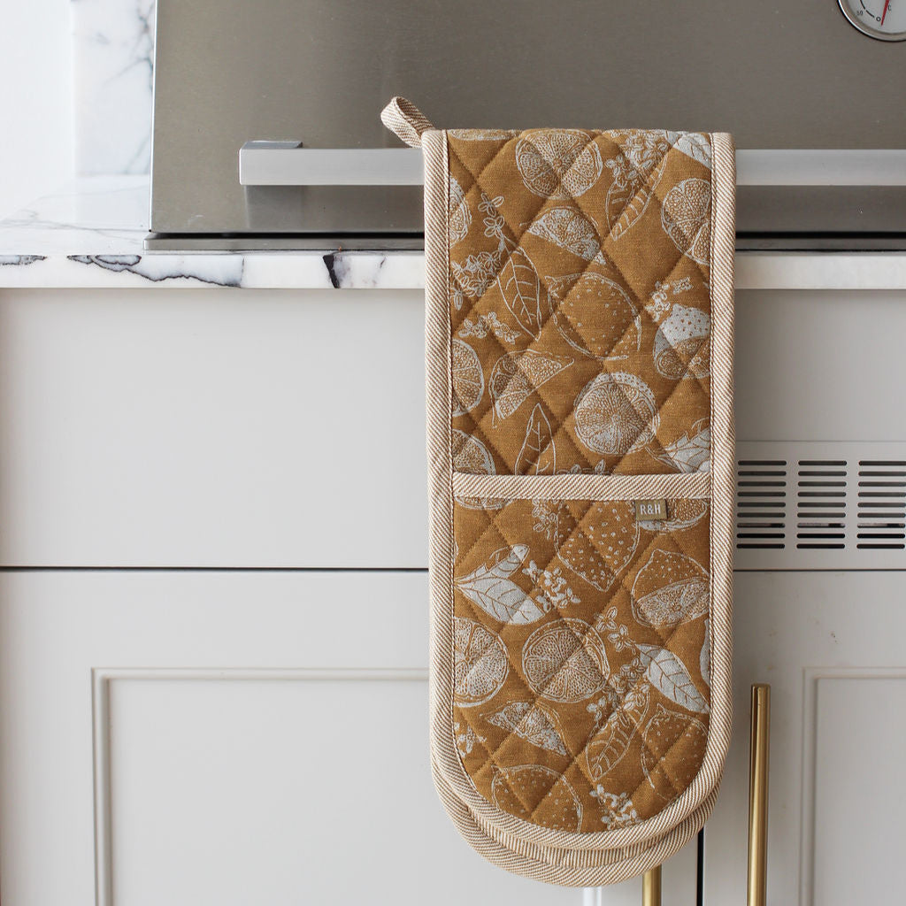 Quilted mustard oven mitt hanging on a kitchen cabinet with marble backsplash
