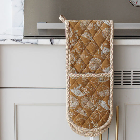 Quilted mustard oven mitt hanging on a kitchen cabinet with marble backsplash