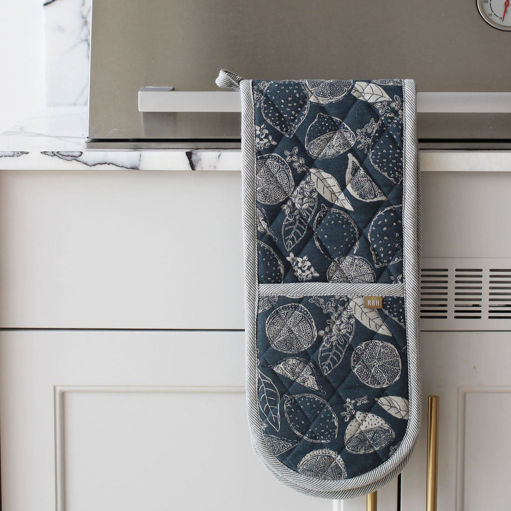 Blue Oven mitt with lemon, leaf pattern hanging on a kitchen cabinet handle.