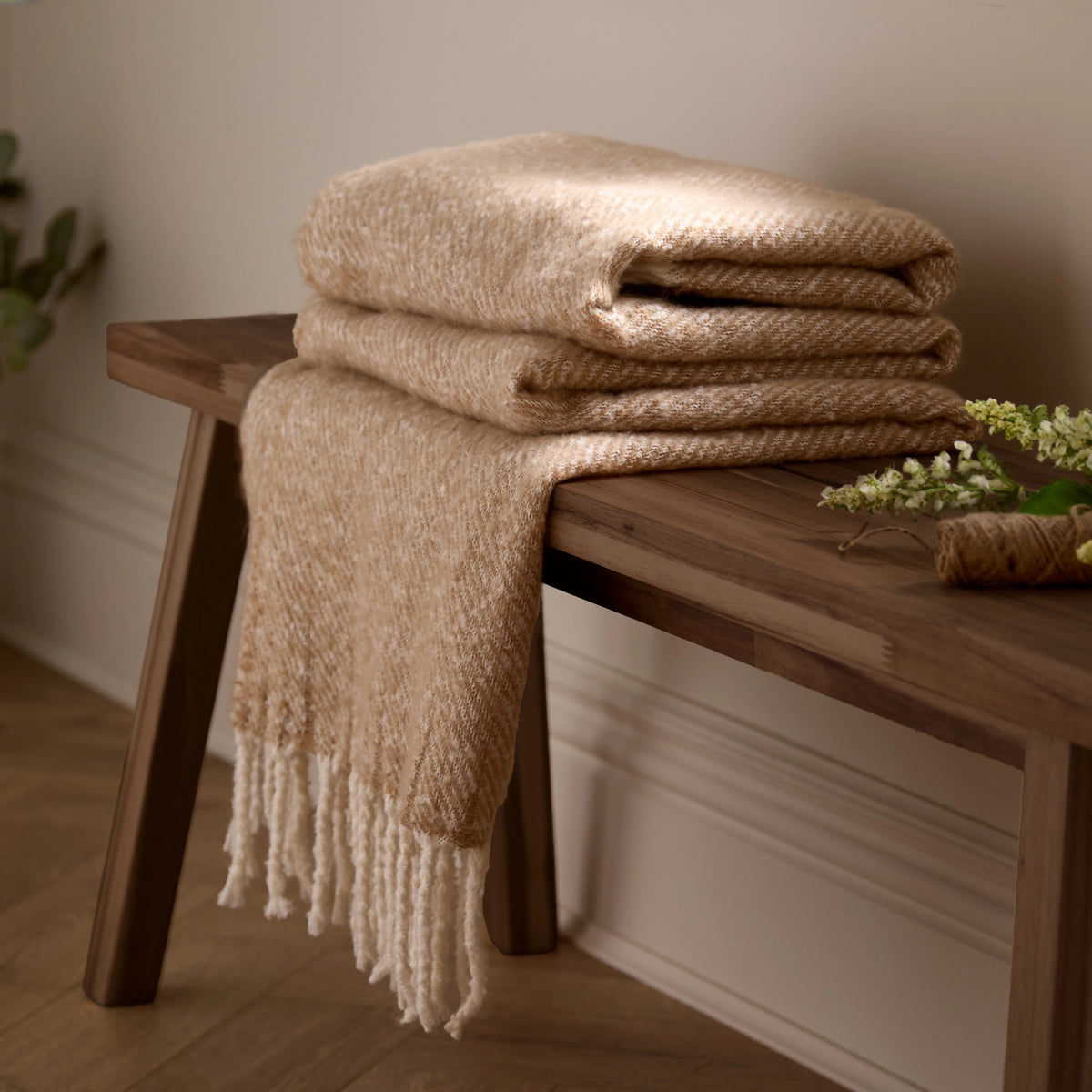 Folded beige blanket on a wooden bench with a neutral background