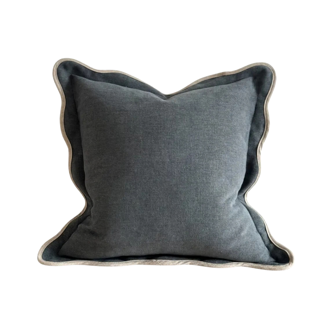 A square cushion in a textured washed navy fabric, featuring a cream scalloped edge.