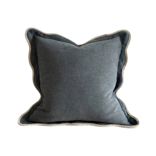 A square cushion in a textured washed navy fabric, featuring a cream scalloped edge.