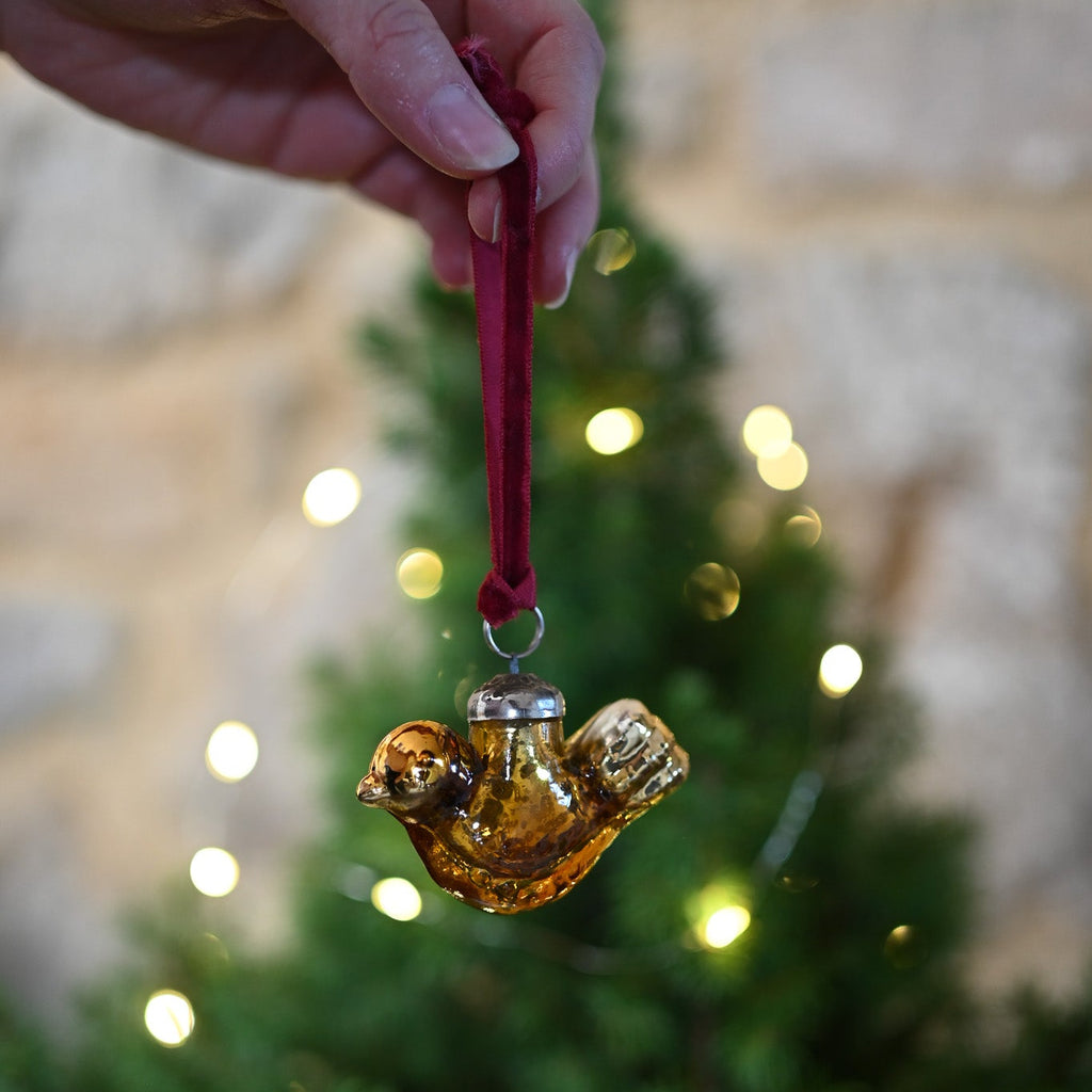 Hand holding a glass bird in front of a Christmas tree with lights.