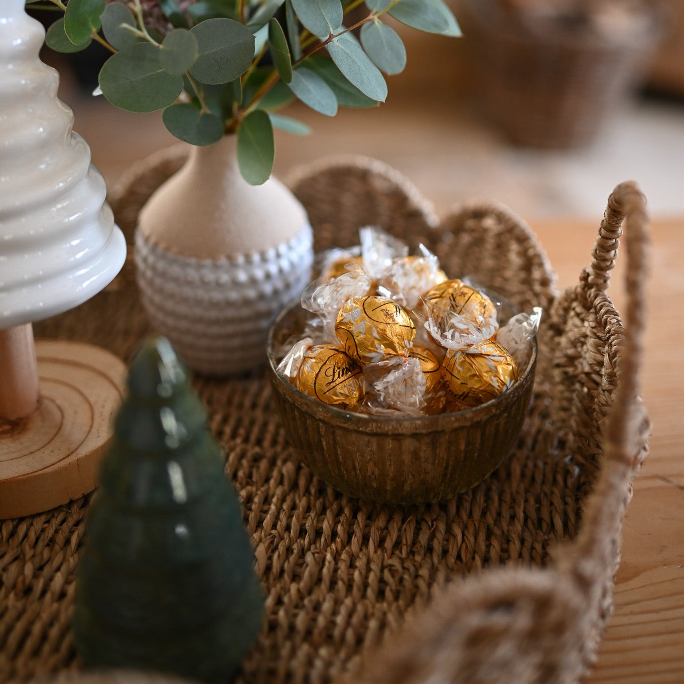 Decorative setting with a vase of greenery, small bowl with decorative items, and a candle on a textured surface.