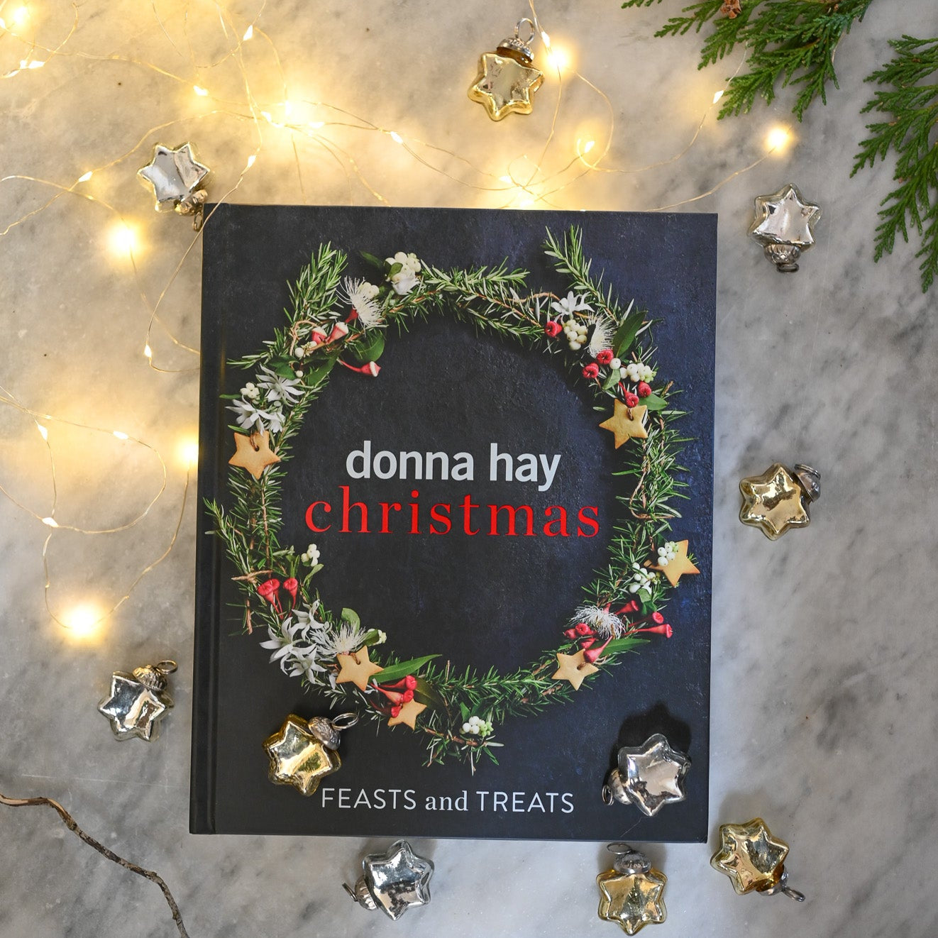 Book titled 'Christmas Feasts and Treats' by Donna Hay on a decorative background with lights and greenery.