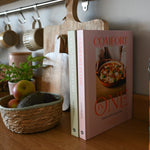 Load image into Gallery viewer, Cookbook titled &#39;Comfort One&#39; on a wooden surface with kitchen items in the background

