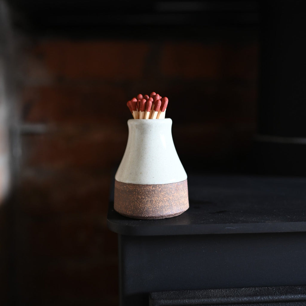 Ceramic milk bottle with matches on a fireplace.