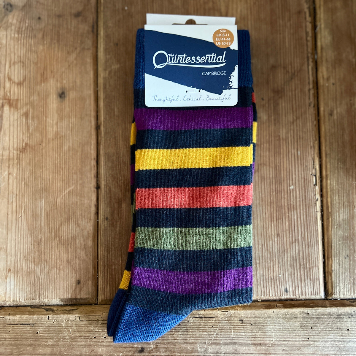 Colourful striped men's sock with a 'Quintessential Cambridge' label on a wooden surface