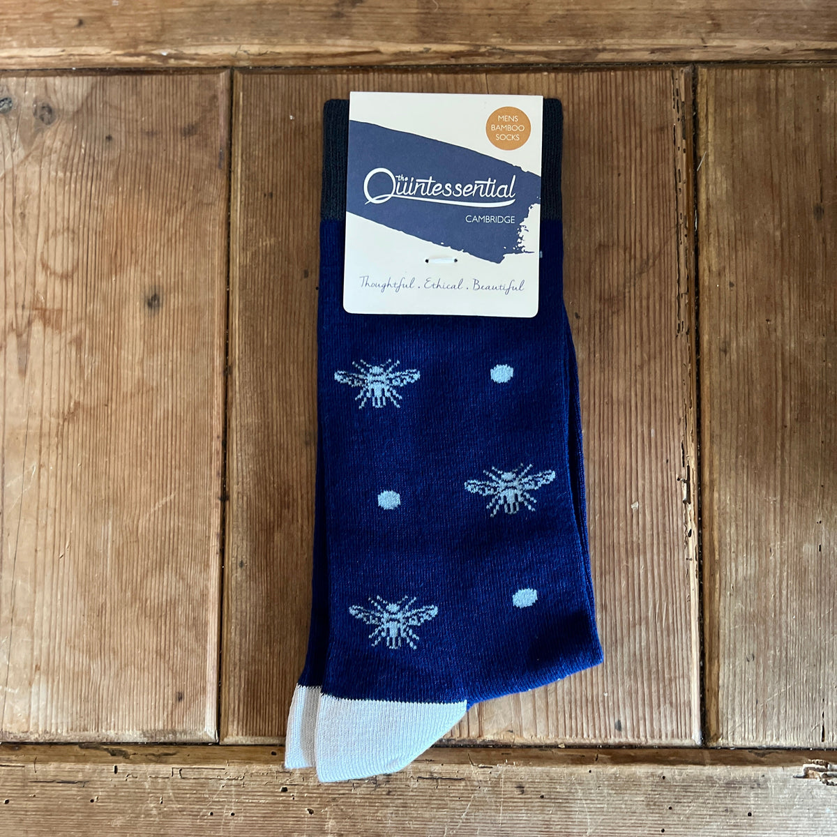 Pair of blue socks with bee patterns on a wooden surface, featuring a brand label.