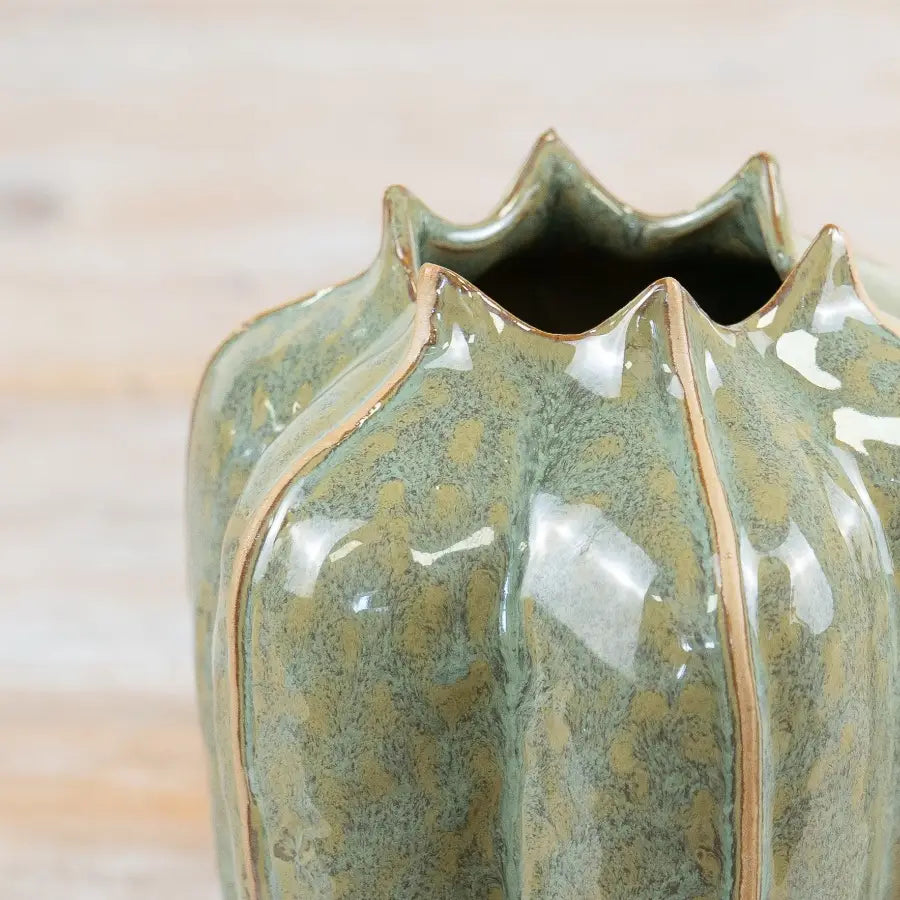Close-up of a glossy ceramic vase with a scalloped rim, featuring a textured sage green and olive glaze with subtle gold-toned speckling and a thin gold line detail, set against a light wood background.