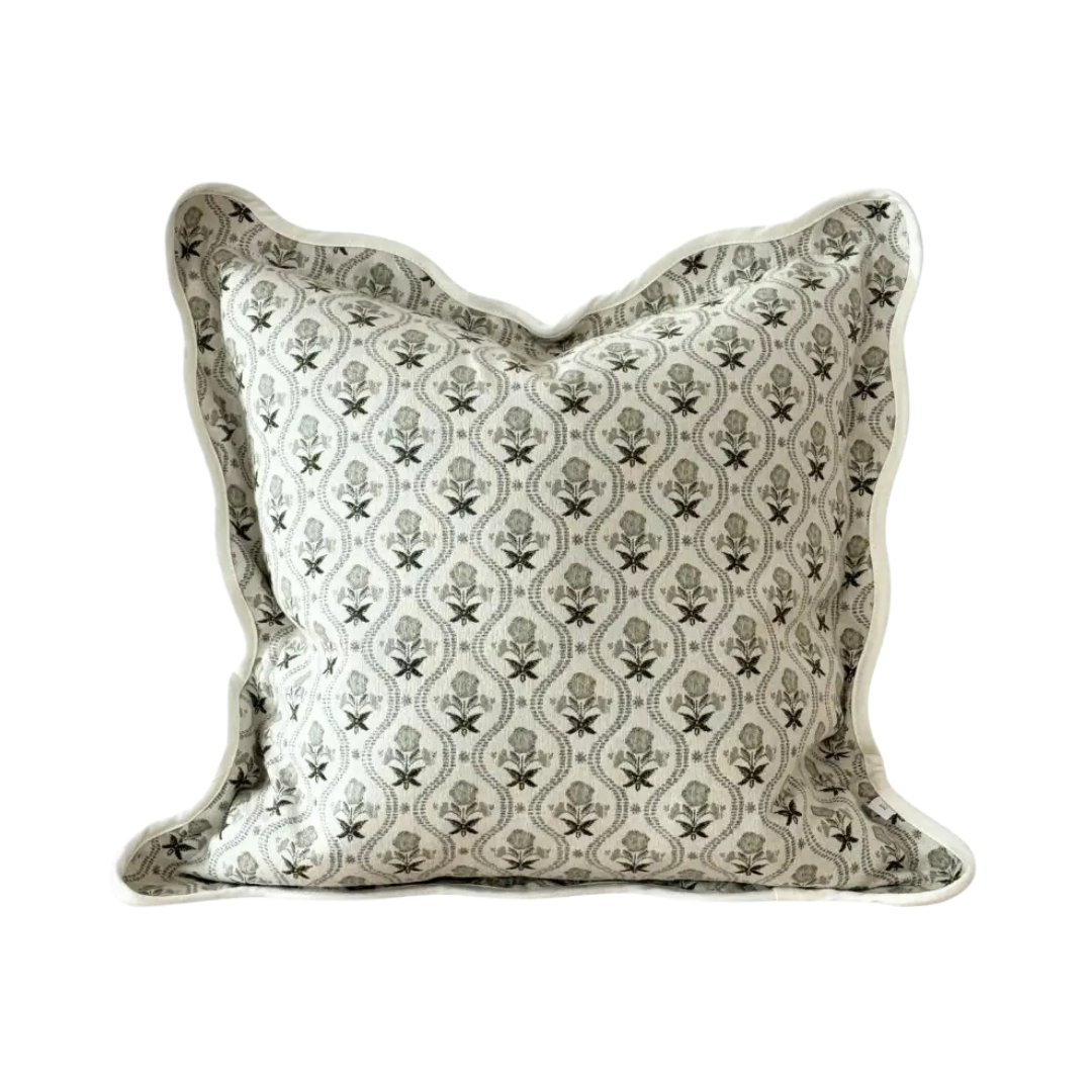 A square decorative cushion with a green and off-white floral trellis pattern and a scalloped edge, shown on a off white background.