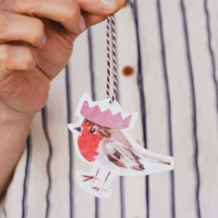 Hand holding a decorative paper clip with a cartoon robin design against a striped shirt background