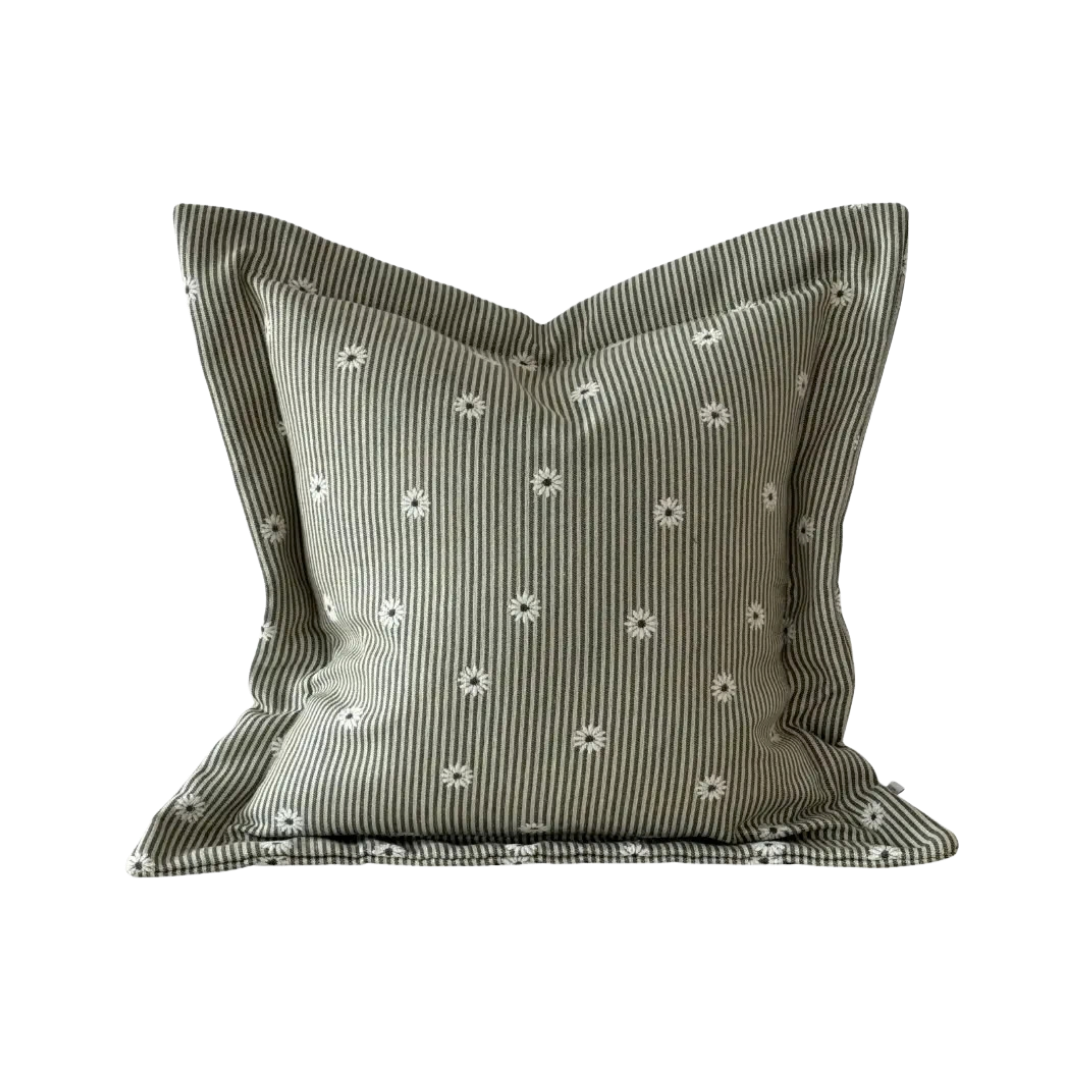 A square cushion in a muted sage green fabric with thin vertical white stripes and small white embroidered daisy motif, shown against a plain cream background.