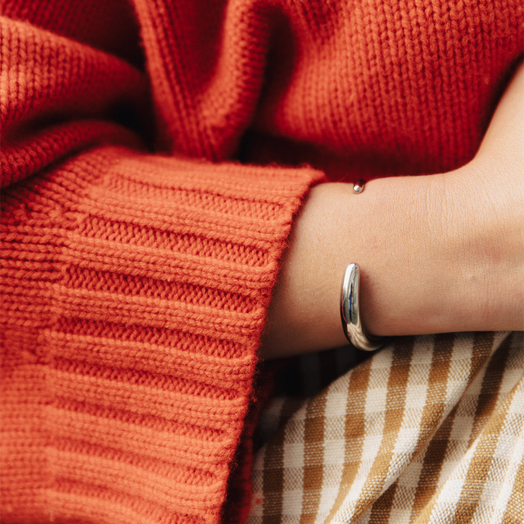 Close-up of a person wearing a silver bangle with a red sweater and plaid fabric in the background