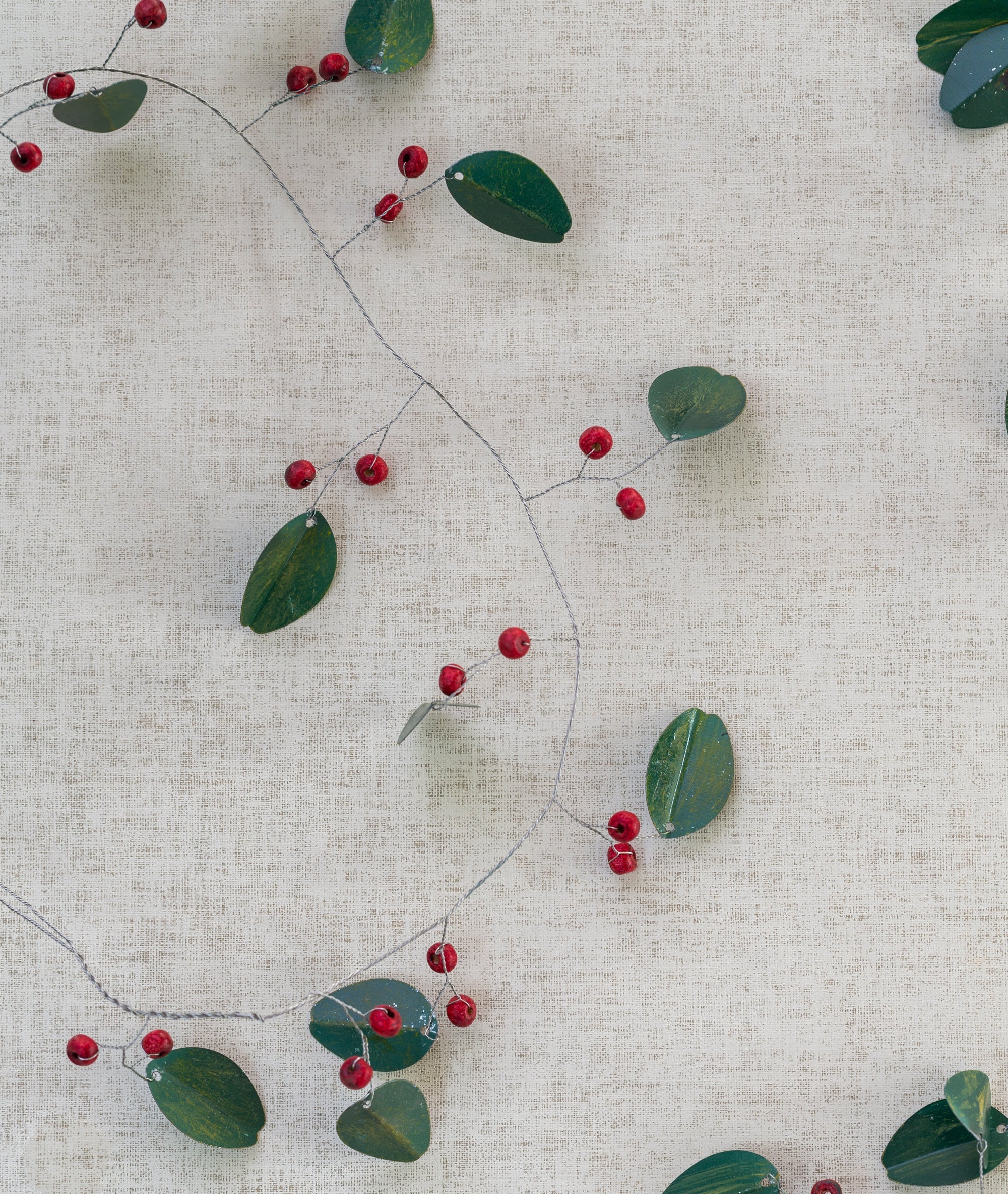 Decorative string with green leaves and red berries on a textured beige background