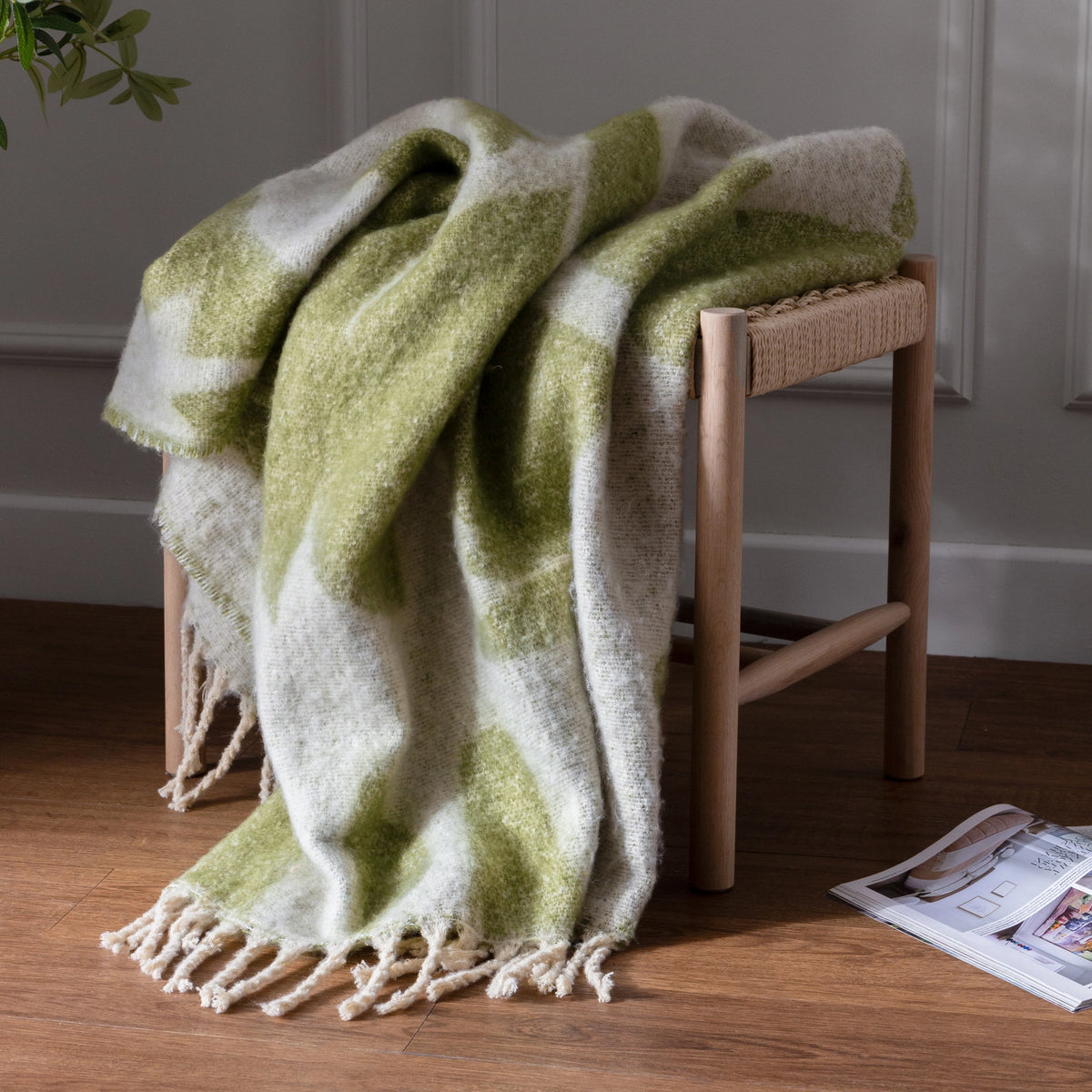 Green and white patterned blanket draped over a wooden stool on a wooden floor.