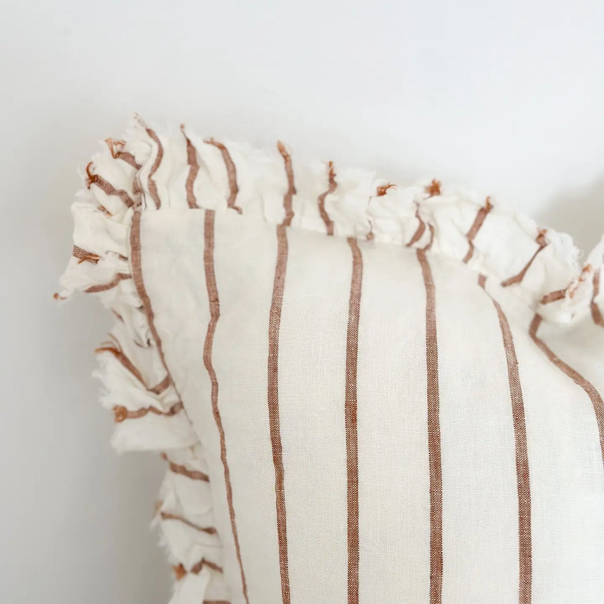Close-up of a textured off-white cushion with vertical brown stripes and a fringed ruffle trim along the edge, set against a plain white background.