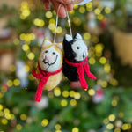 Load image into Gallery viewer, Two small felt cat decorations with scarves held against a blurred Christmas tree background.
