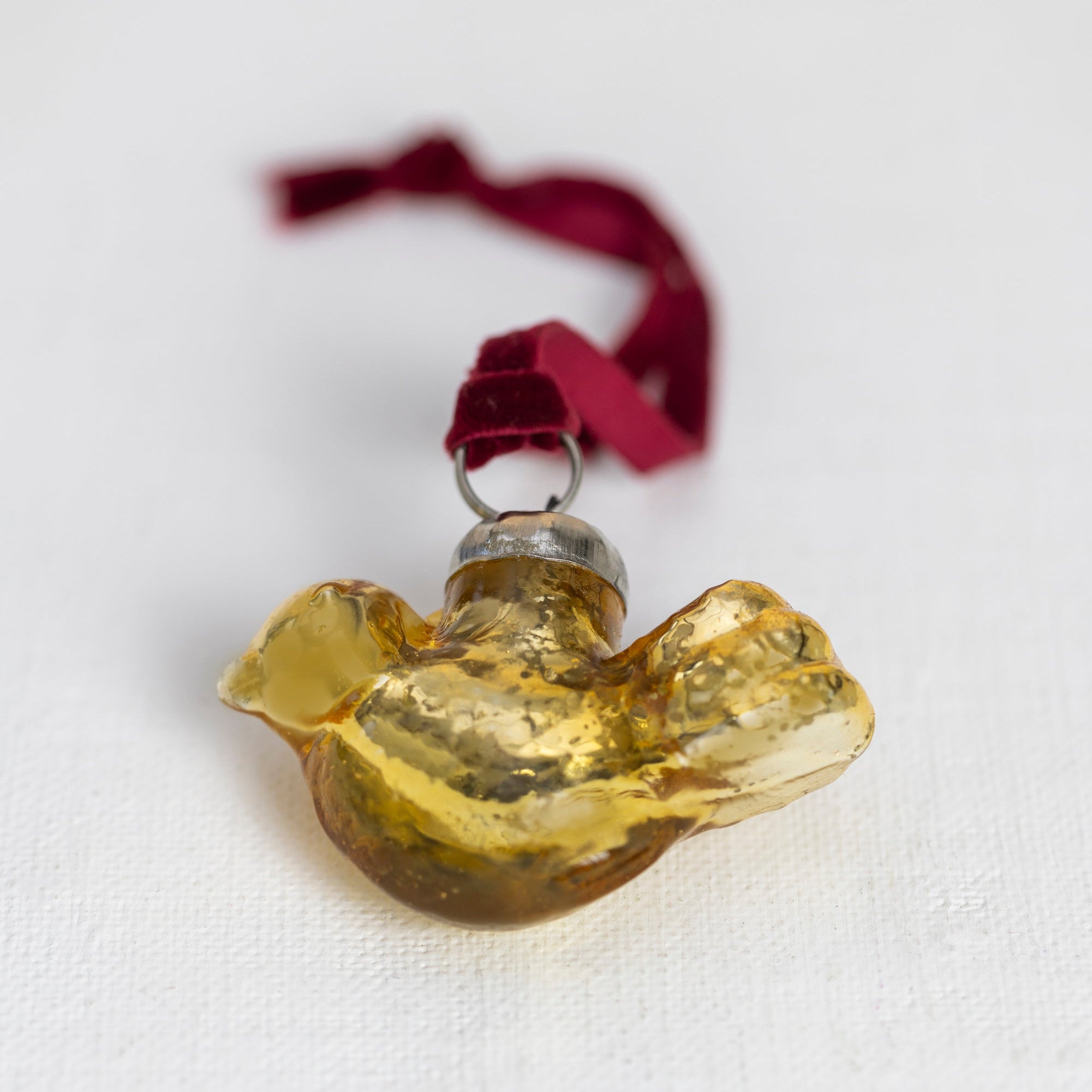 Gold glass dove ornament with red ribbon on a white background