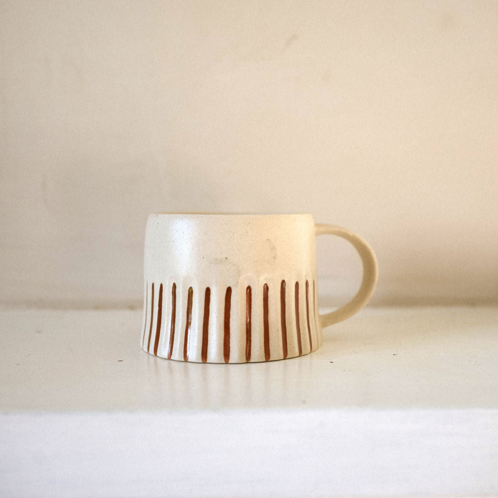 Ceramic mug with ginger coloured stripes on a white surface against a beige background