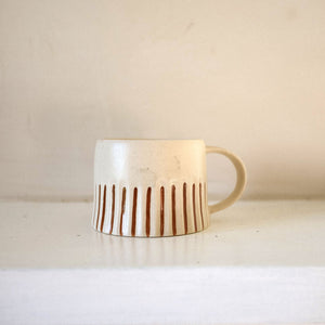 Ceramic mug with ginger coloured stripes on a white surface against a beige background