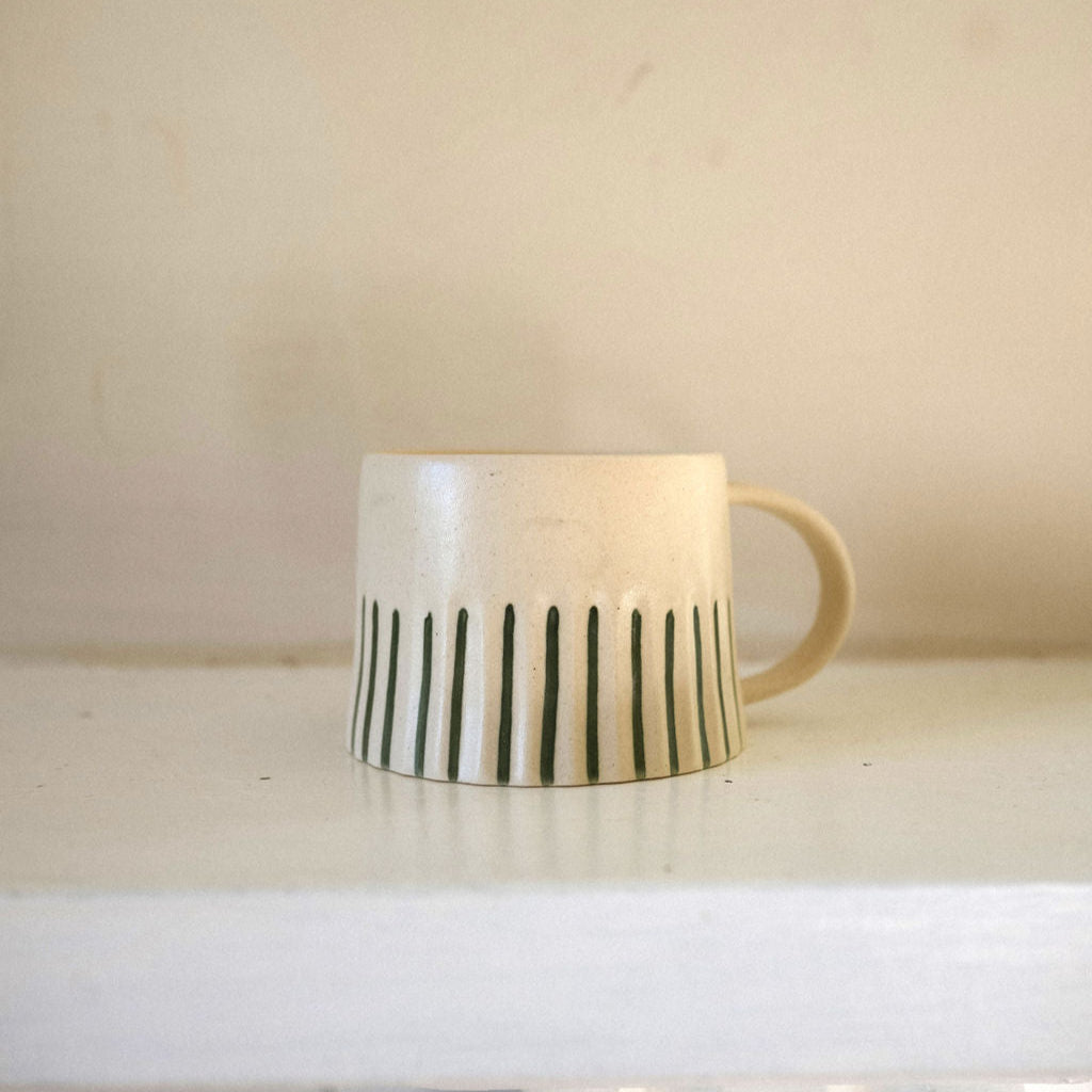 Ceramic mug with green stripes on a white surface against a beige wall