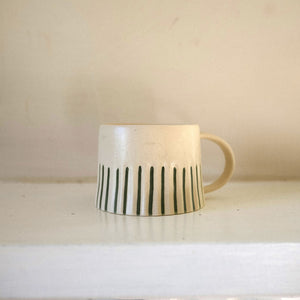 Ceramic mug with green stripes on a white surface against a beige wall