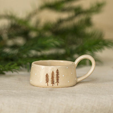 Small ceramic t-light holder on a table with decorative lights and greenery in the background