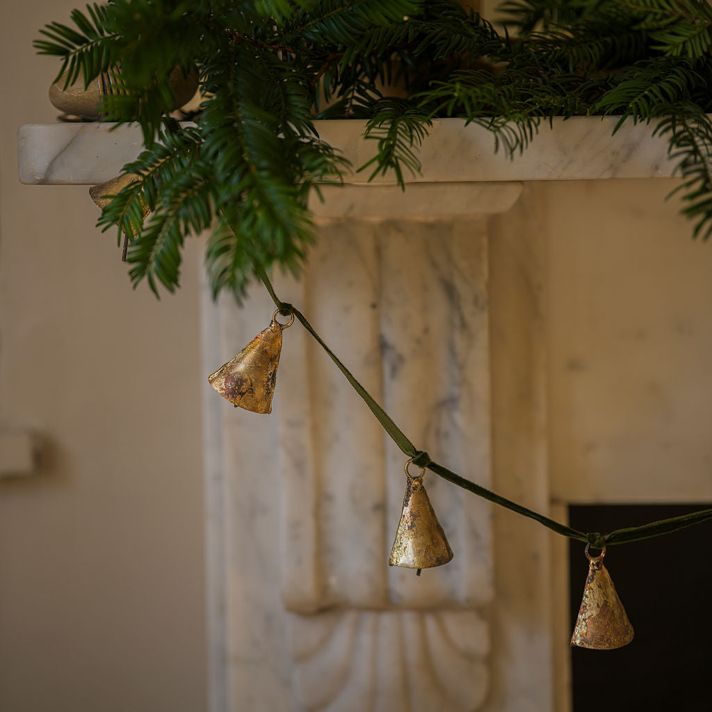Decorative gold bell garland hanging from a branch with a marble fireplace in the background