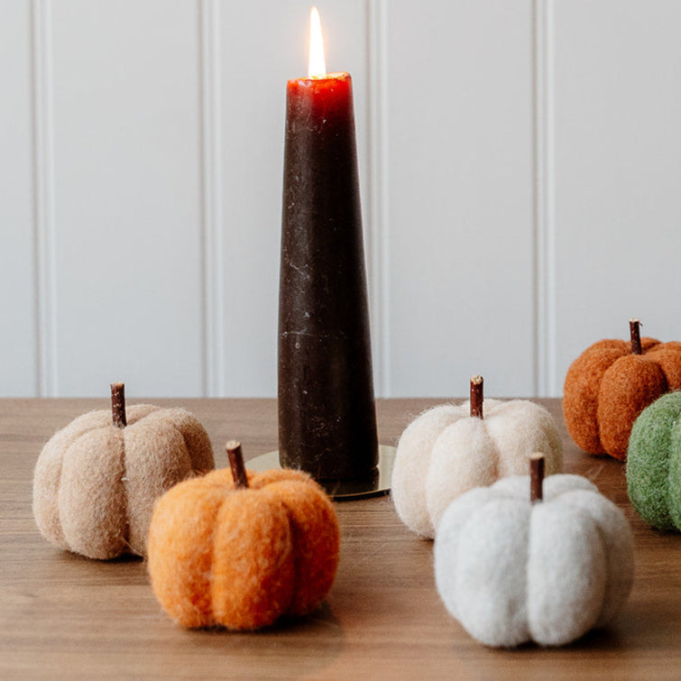 Decorative felt pumpkins on a wooden surface with a white paneled wall background.