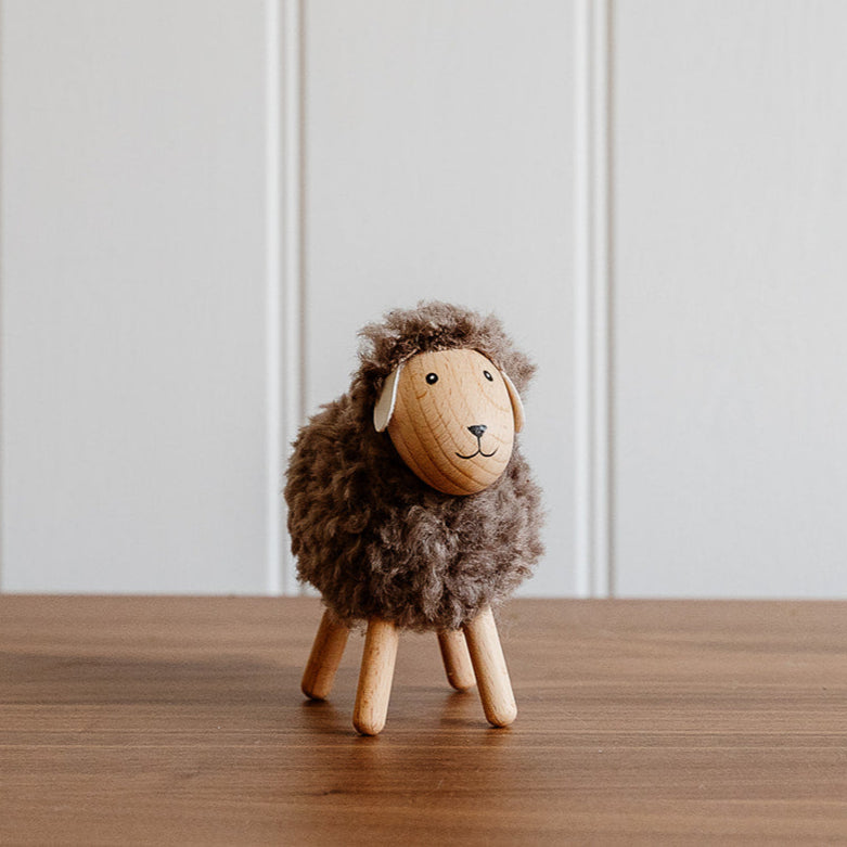 Small wooden sheep figurine on a wooden surface with a white paneled wall background