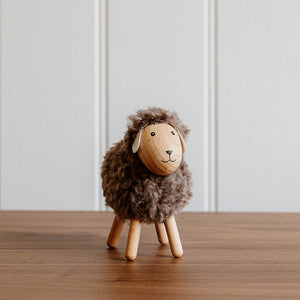 Small wooden sheep figurine on a wooden surface with a white paneled wall background