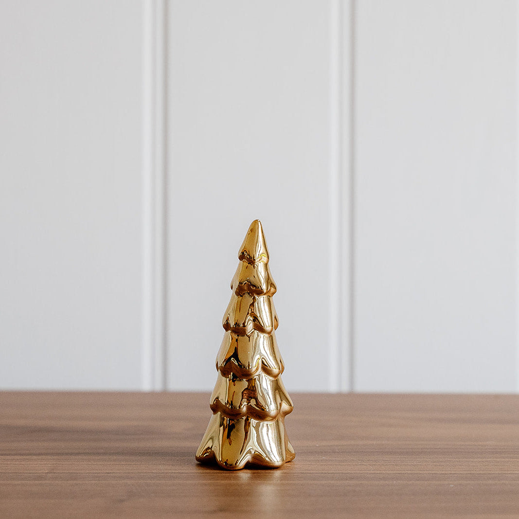 Gold Christmas tree ornament on a wooden surface with a white paneled background