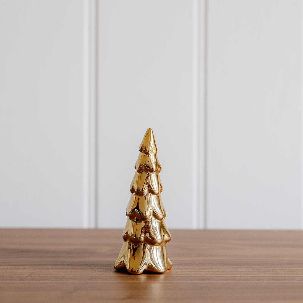Gold Christmas tree ornament on a wooden surface with a white paneled background