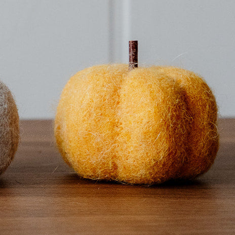 Felt decorative pumpkin on a wooden surface with a light grey wall background.