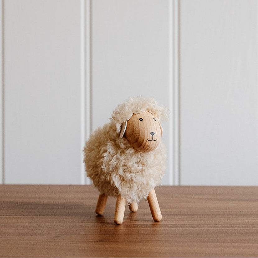 Small sheep figurine on a wooden surface with a white paneled wall background