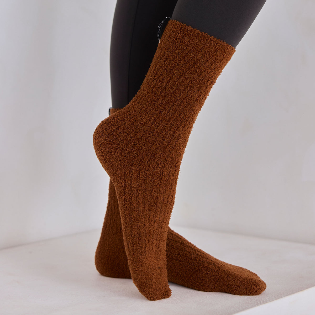 Brown knitted socks worn with black leggings on a white background