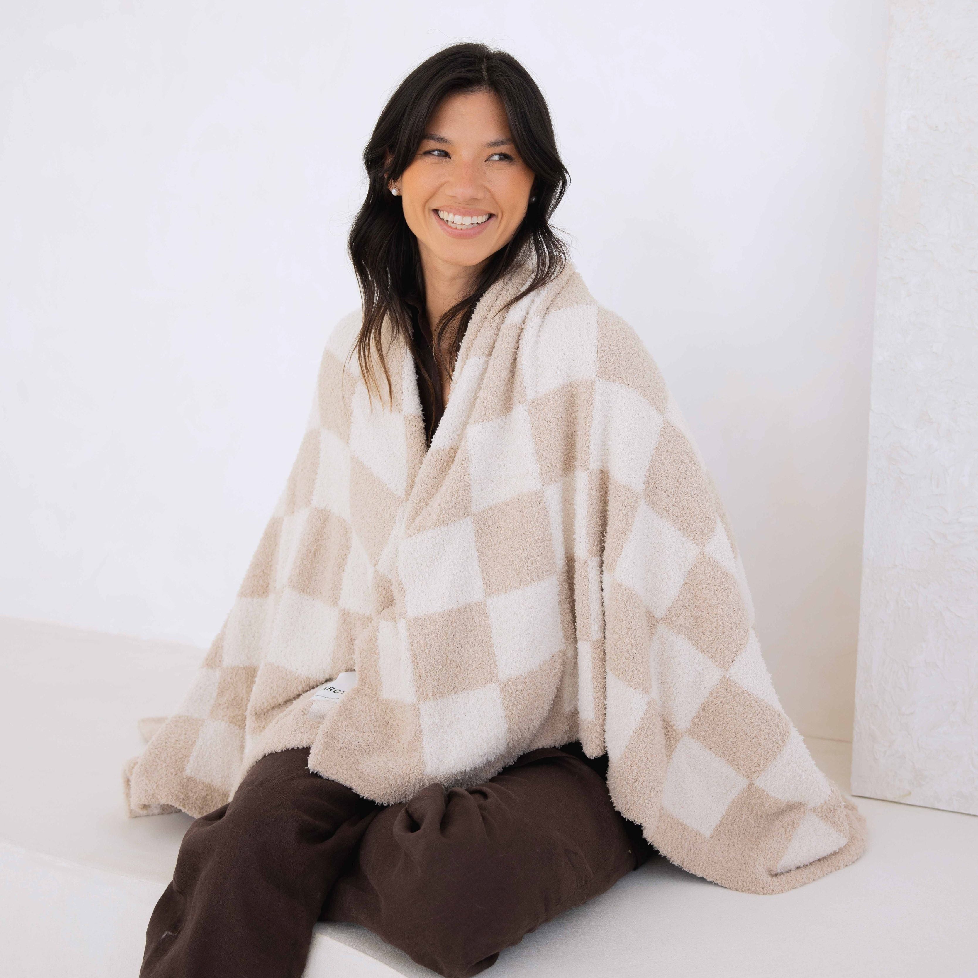 Woman wrapped in a checkered blanket sitting on a white surface