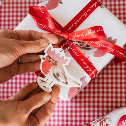Gift wrapped in red and white paper with a red ribbon on a checkered tablecloth.
